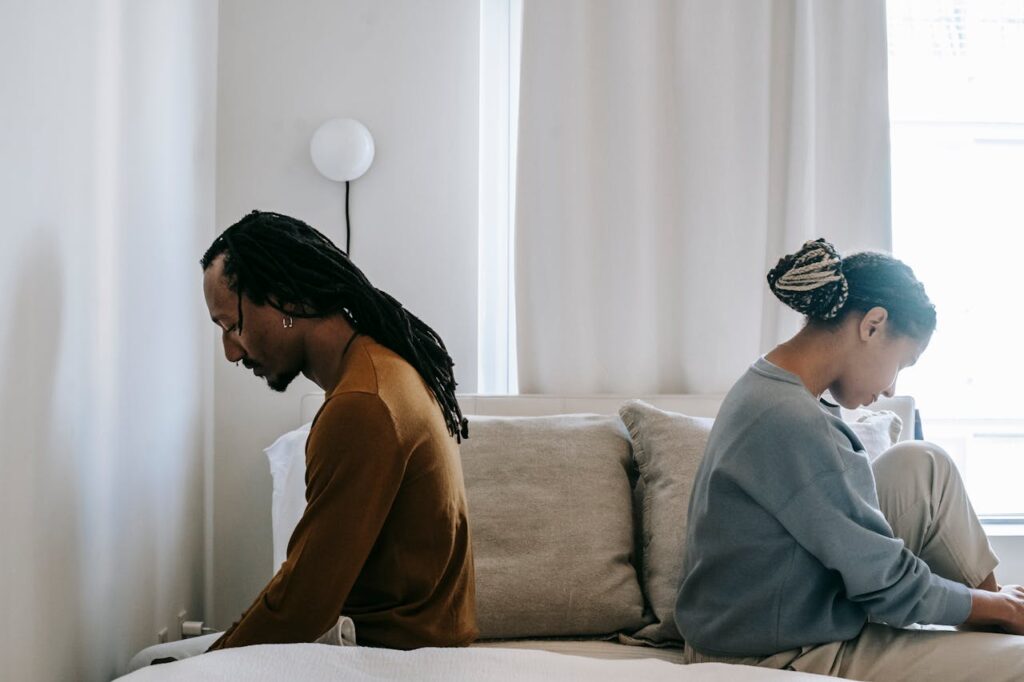 Side view unhappy sorrowful African American couple sitting on bed back to back after having argument